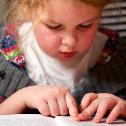 Girl reading book while moving her finger