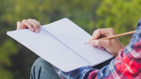 View of person's hands writing in notebook