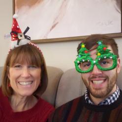 Susan and an adult Justin wearing holiday hats and glasses.
