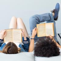 Two teens lying down and reading books.